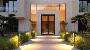A modern building with a central entrance, flanked by well-maintained hedges and a pathway leading to the door. - One room apartment  (Saints Constantine and Helena)