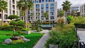 A modern building with a pool, surrounded by well-maintained gardens and palm trees. - One room apartment  (Saints Constantine and Helena)