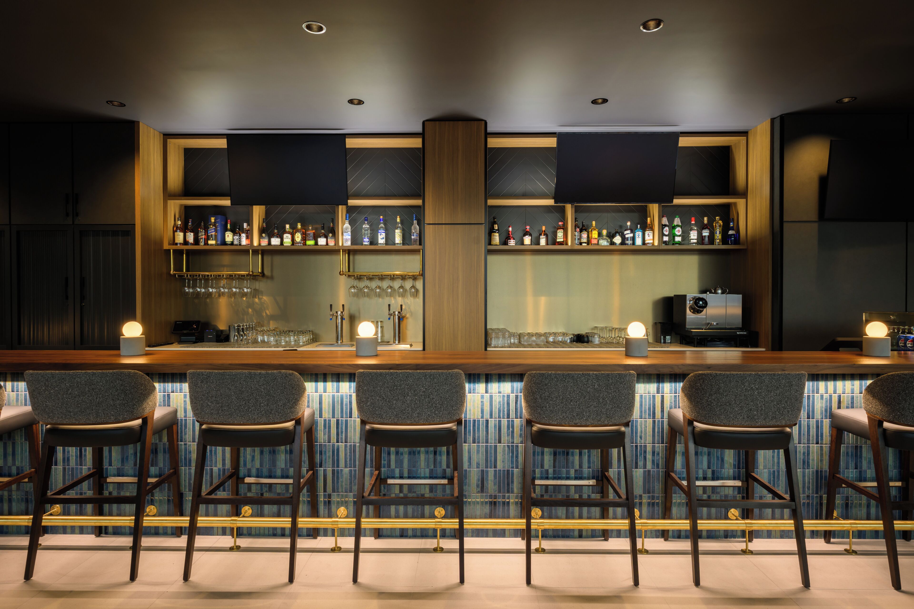 Een bar met meerdere stoelen, planken vol flessen en glazen.