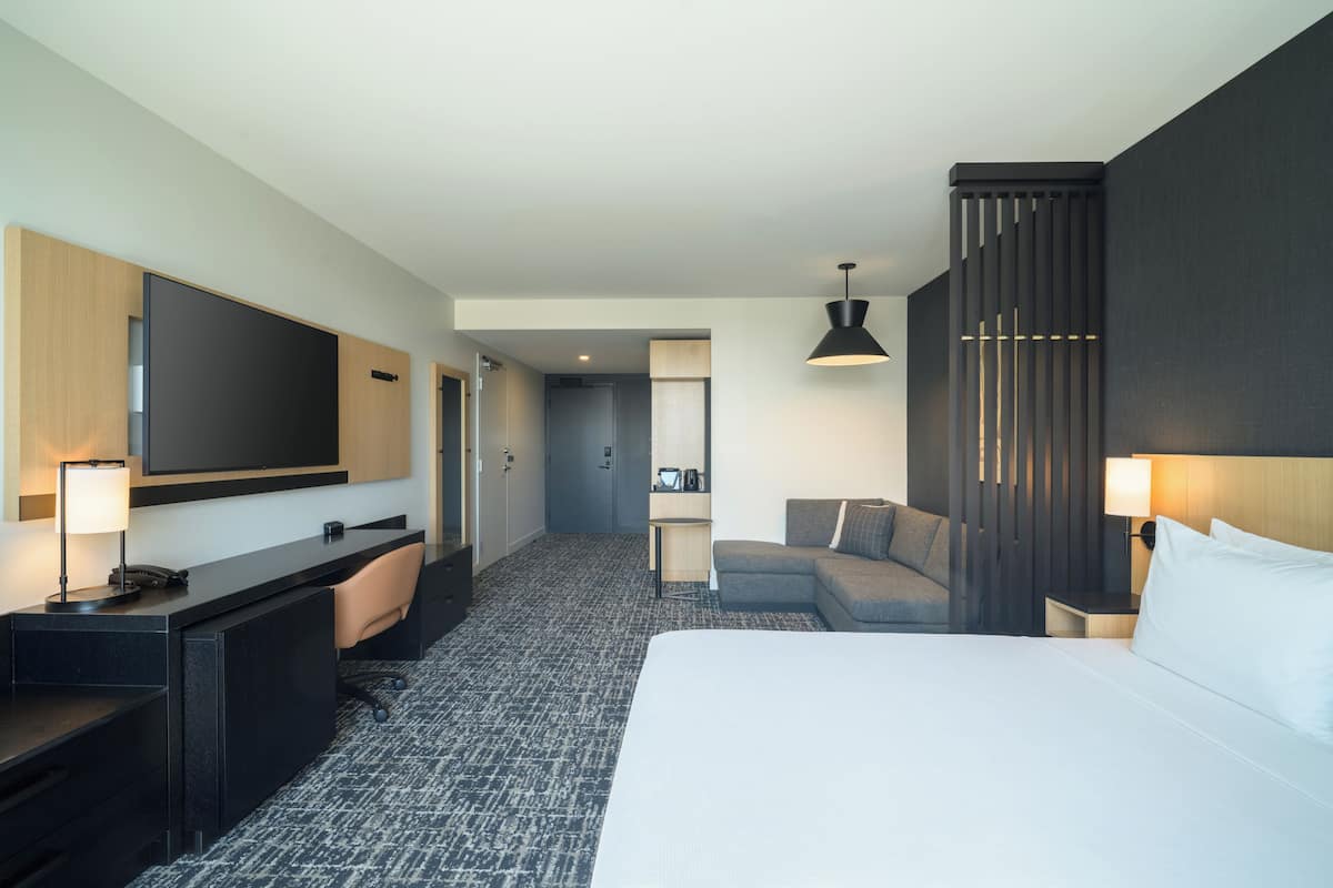 Camera d'albergo con un letto grande, una scrivania con lampada, un divano, una TV a parete e un'area salotto separata con lampada.