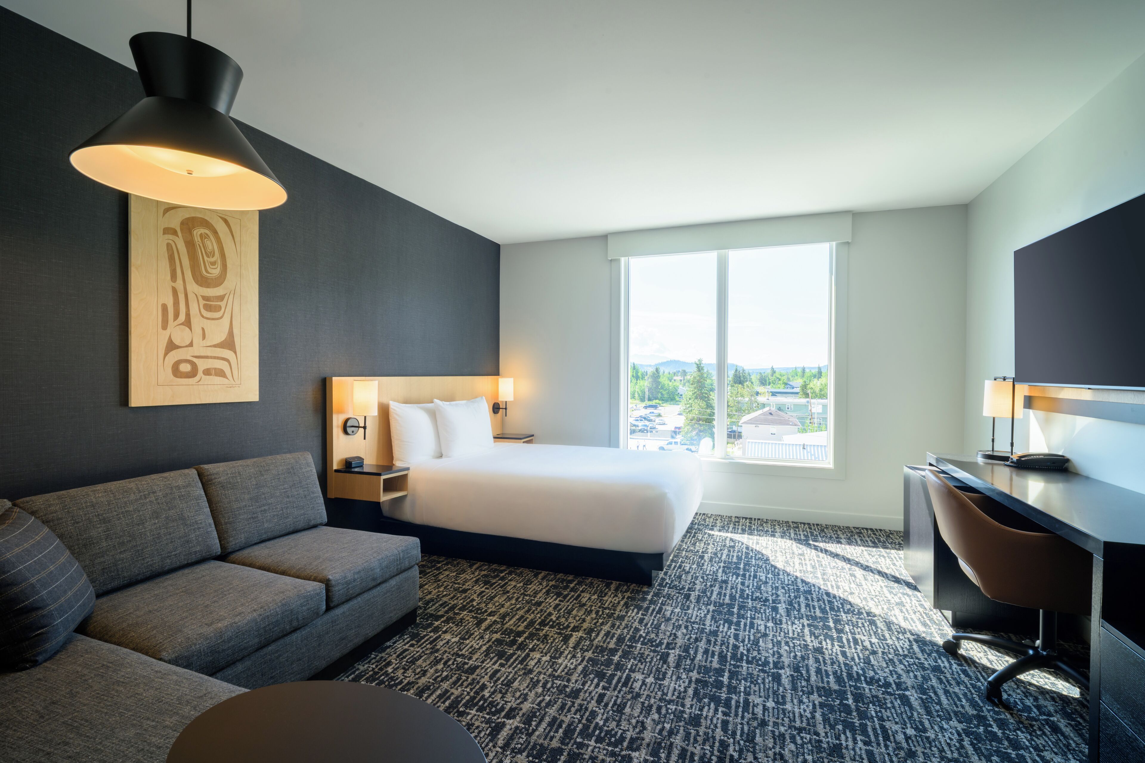 Ein modernes Hotelzimmer mit Bett, Sofa, Schreibtisch und großem Fenster mit Blick auf die Stadt.