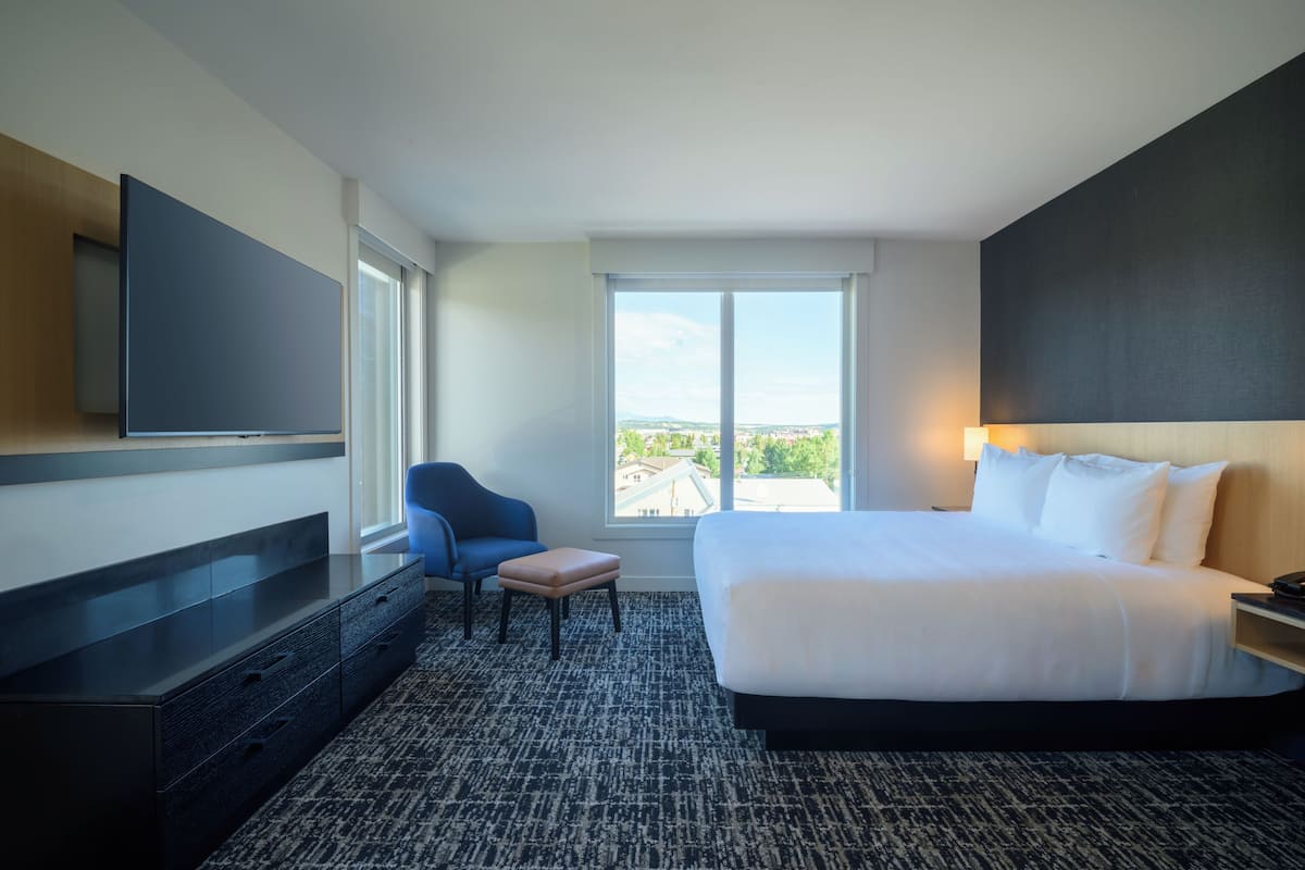 Camera d'albergo con un letto grande, una televisione a muro, una sedia, un tavolino e una finestra con vista.