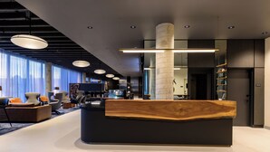 A modern reception area with a wooden reception desk, comfortable seating, and a large window providing natural light. - Hyatt Place Whitehorse (WHITEHORSE)