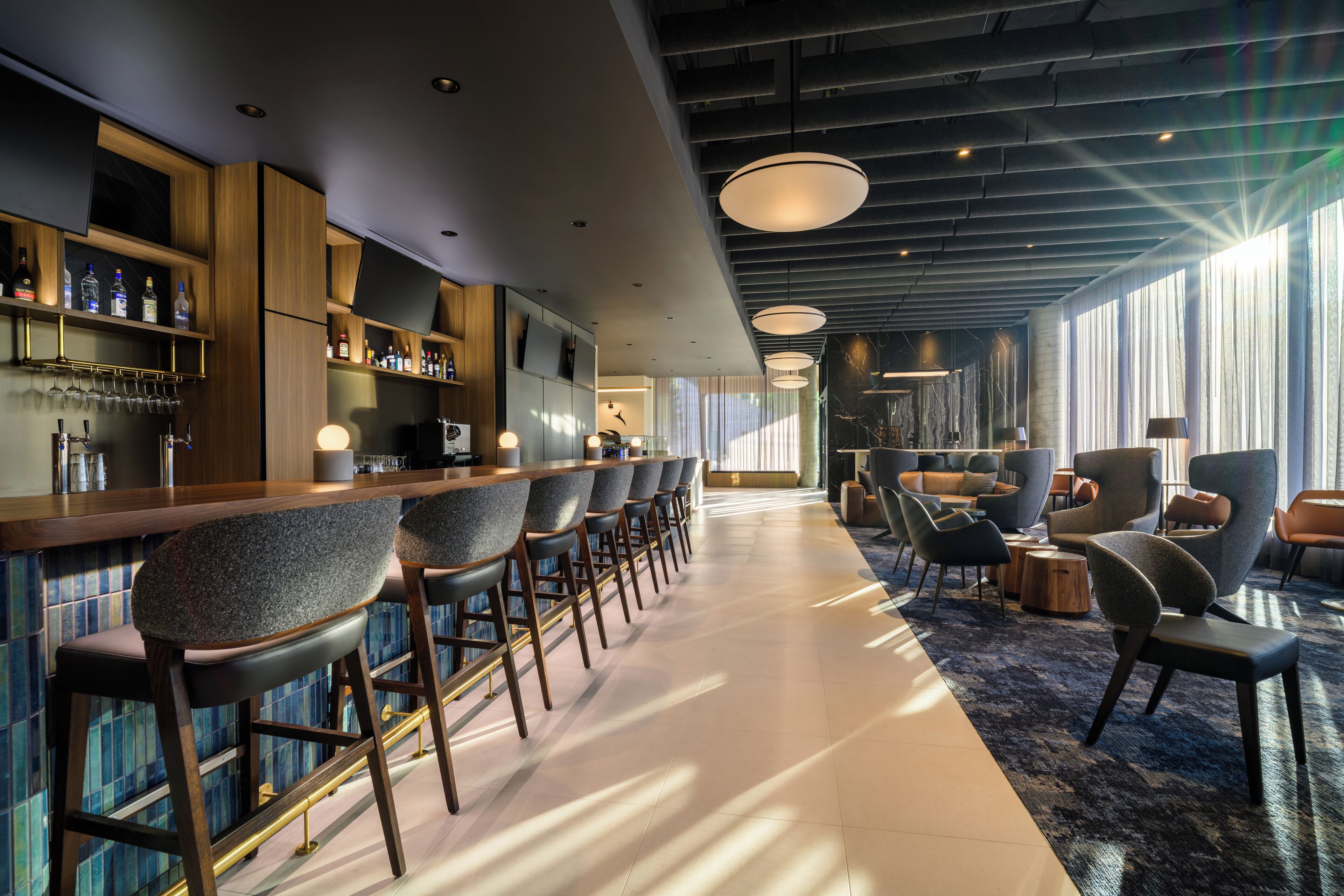 Un área de bar moderna con taburetes altos, una barra y un espacio de estar con sofás y sillones.