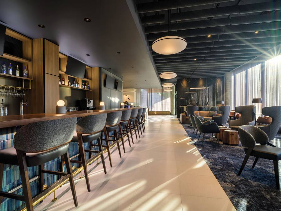Un área de bar moderna con taburetes altos, una barra y un espacio de estar con sofás y sillones.