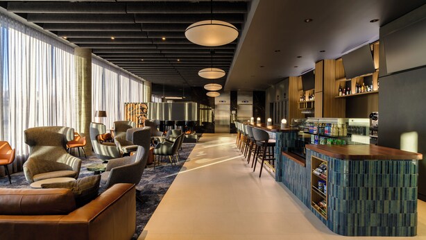 A modern hotel lobby with a bar area, seating arrangements, and a large window providing natural light. - Hyatt Place Whitehorse (WHITEHORSE)