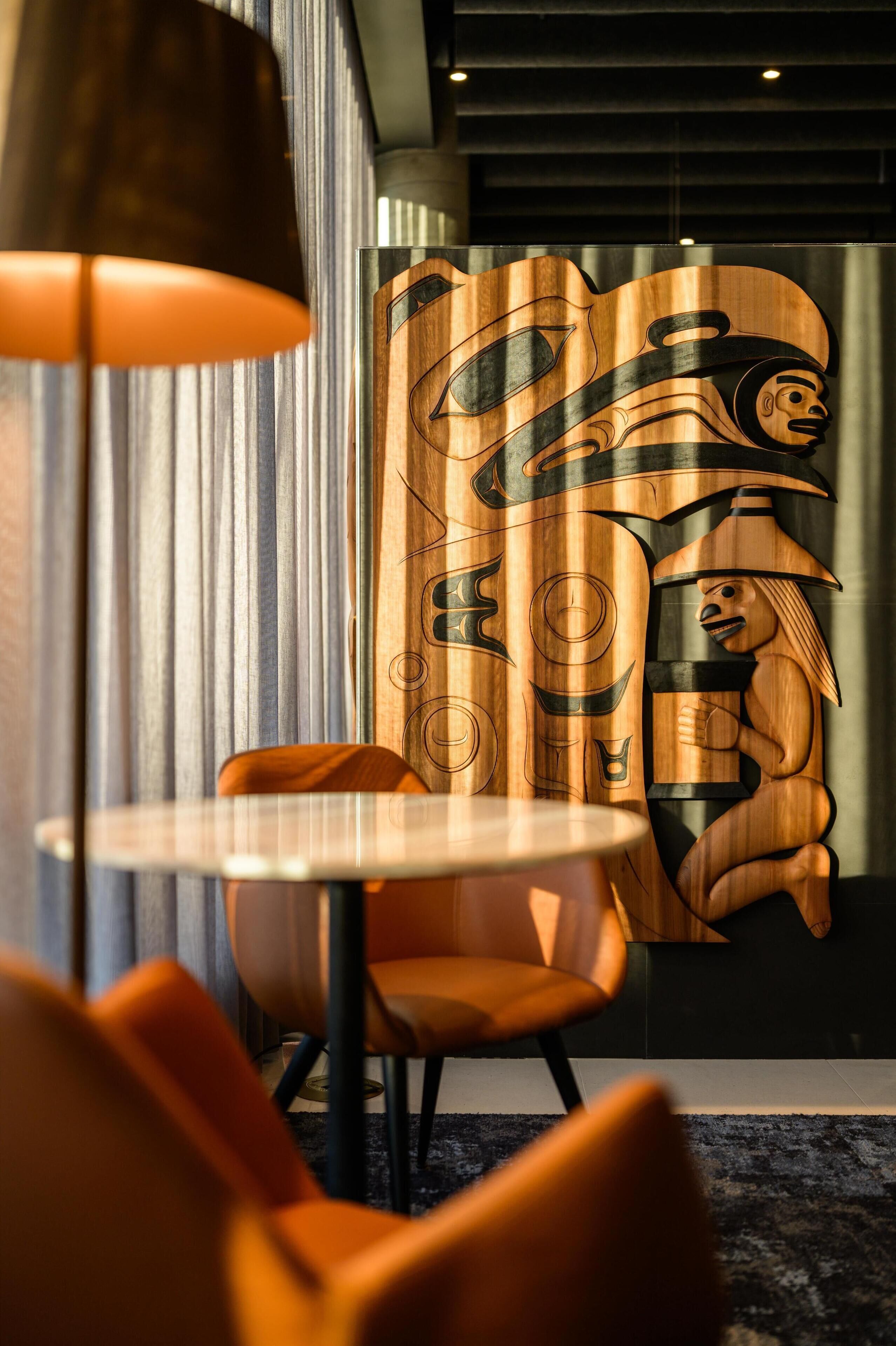Un interior moderno con una mesa redonda, sillas naranjas y una obra de arte de madera en la pared.
