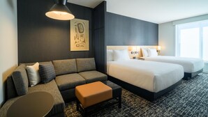 A hotel room with a sofa, two beds, a coffee table, and a large window. - Hyatt Place Whitehorse (WHITEHORSE)