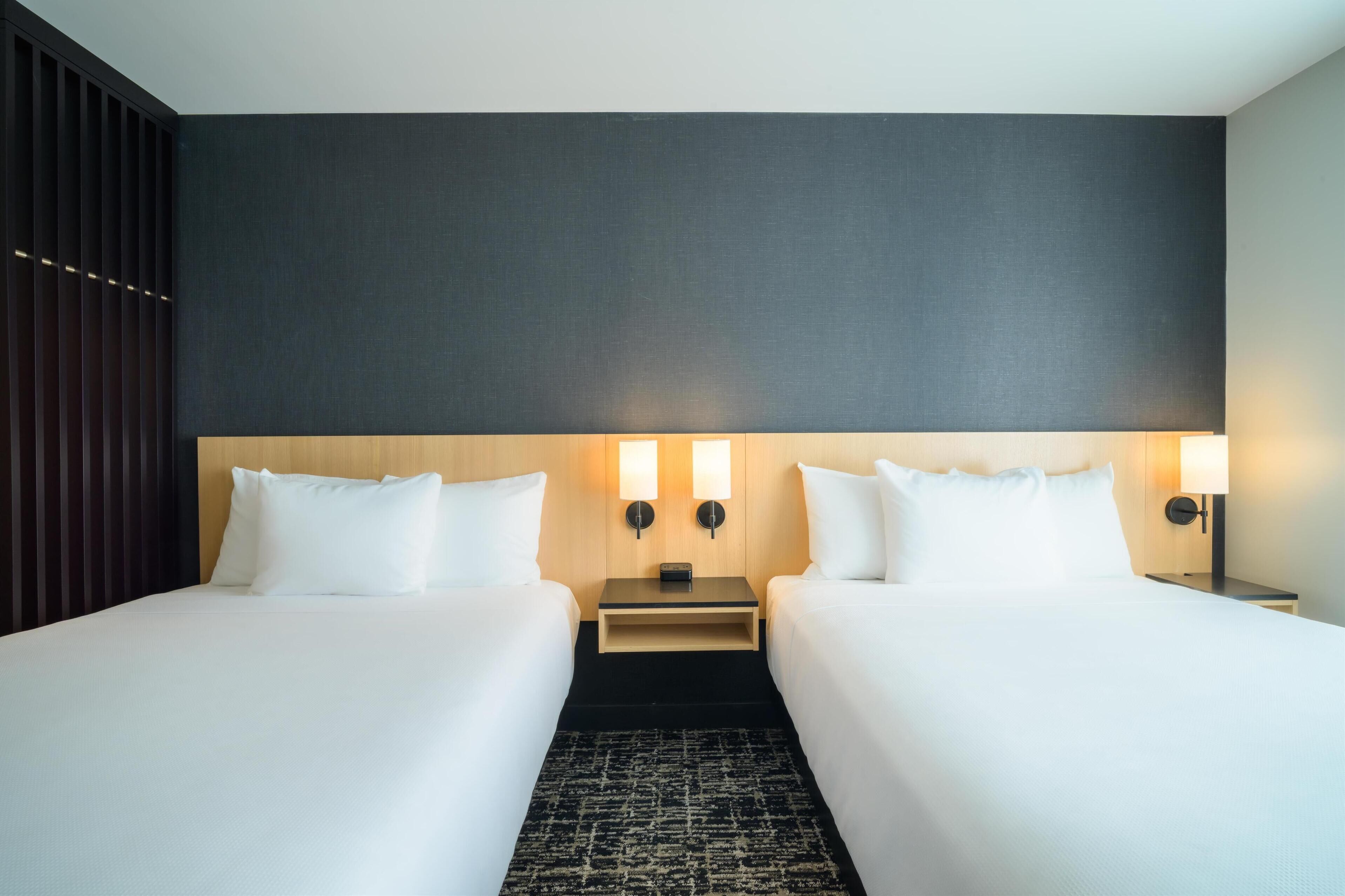 Een hotelkamer met twee bedden, een donkere wand en twee wandlampen.