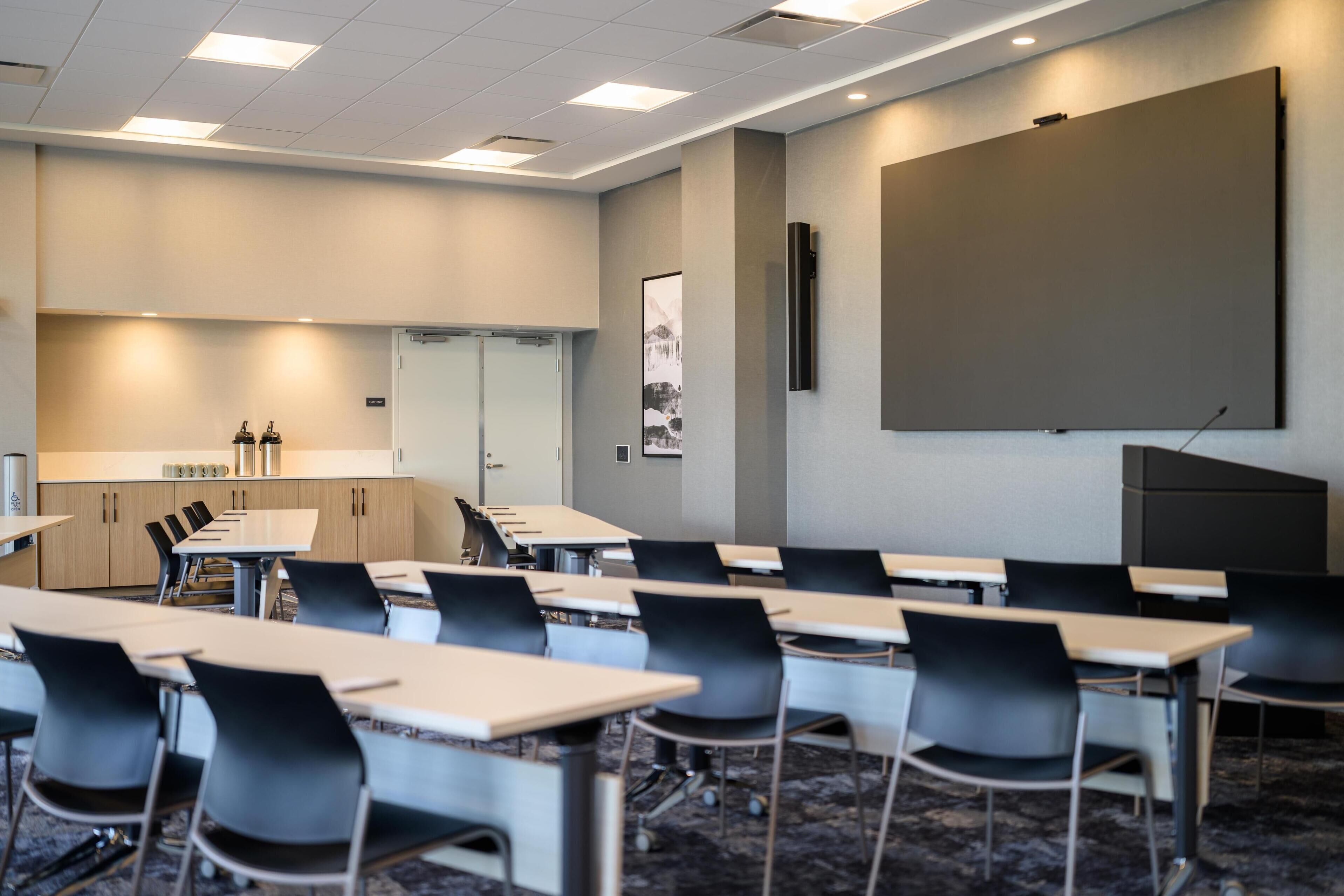 A conference room with tables and chairs, a projector screen, and a large whiteboard.