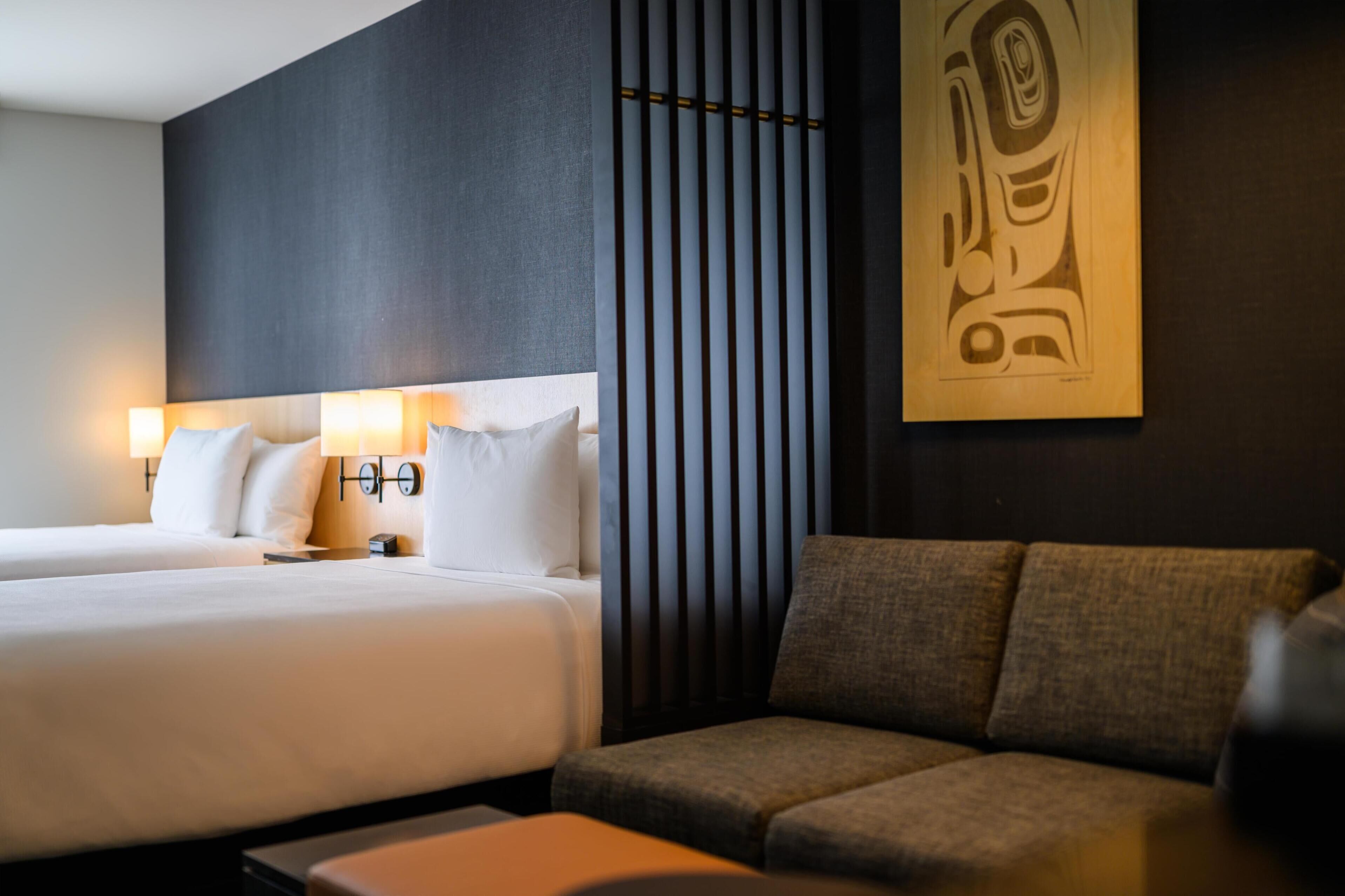A hotel room with a large bed, a sofa, and a wall-mounted artwork.