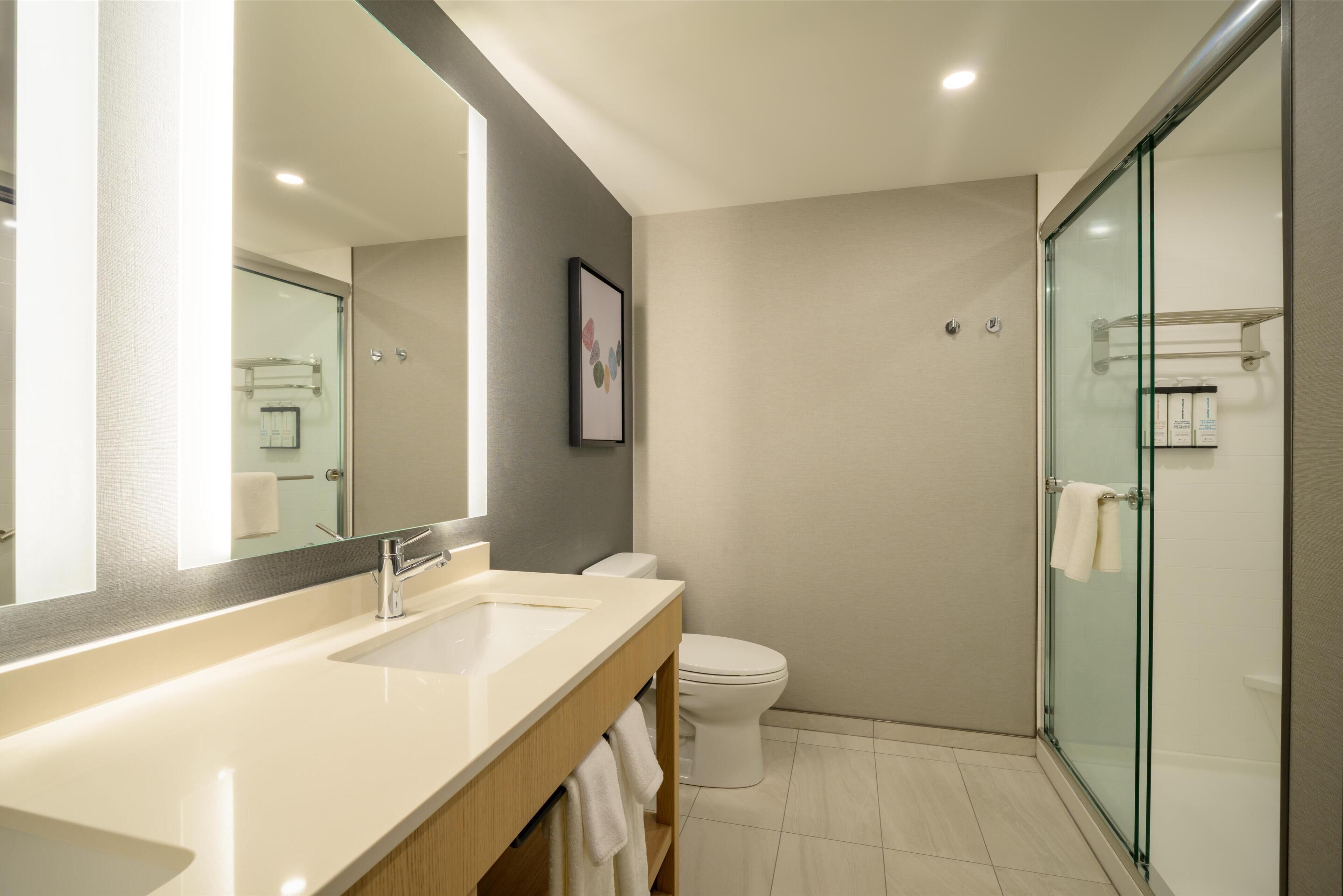 Een moderne badkamer met een grote spiegel, een wastafel, een toilet en een douchecabine van glas.