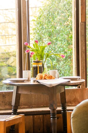 A wooden table with a vase of pink tulips, a coffee pot, a cup, and croissants. - Cabbage Patch - sleeps 2 guests  in 1 bedroom (Rhoscolyn)