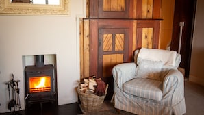 Une pièce chaleureuse avec un poêle à bois, un panier en osier rempli de bois de chauffage et un fauteuil à rayures.