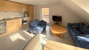 Un espacio habitable compacto con kitchenette, dos sofás estampados, una mesa de centro de madera y un televisor.