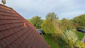 A view of a house with a red-tiled roof and a chimney, surrounded by trees and parked cars. - Fantastic vacation apartment directly on the dike (Wurster Nordseeküste)