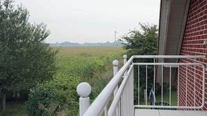 A balcony with a view of a field and wind turbines in the distance. - Fantastic vacation apartment directly on the dike (Wurster Nordseeküste)