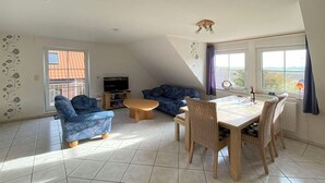 A living room with a dining table, two sofas, a TV, and a window with curtains. - Fantastic vacation apartment directly on the dike (Wurster Nordseeküste)