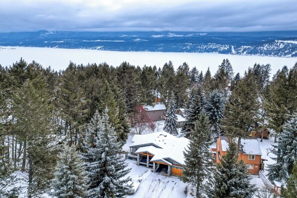 Un chalet enneigé doté d’une grande véranda ouverte, entouré d’une forêt dense de conifères.