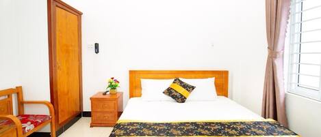 A bedroom with a wooden bed, a nightstand with a vase of flowers, a wooden wardrobe, and a chair.