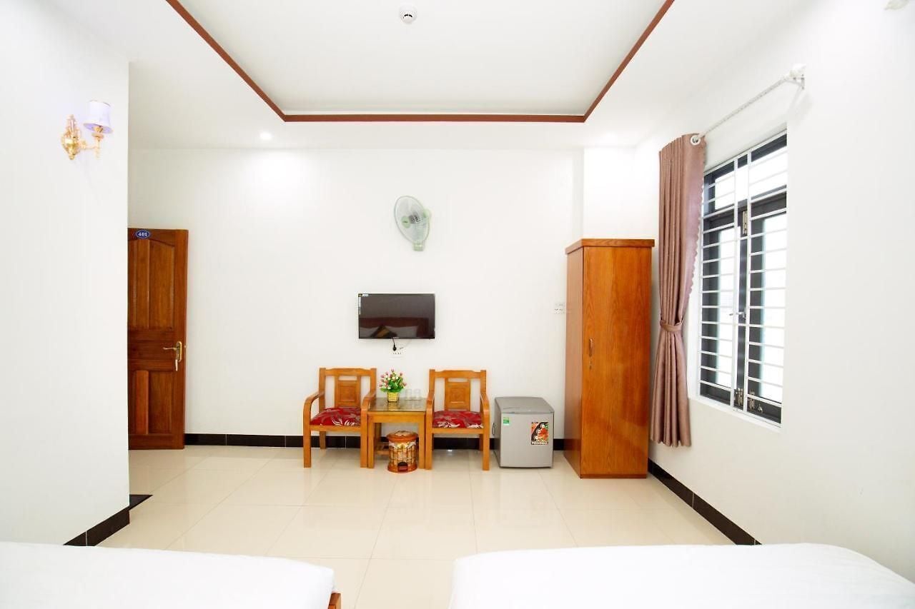 A hotel room with a wooden cabinet, a TV mounted on the wall, a small table with chairs, and a window with curtains.