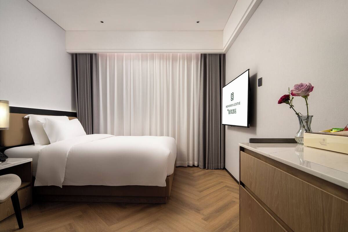 Ein modernes Hotelzimmer mit einem Bett, einem Schreibtisch, einem Fernseher und einer Blumenvase.