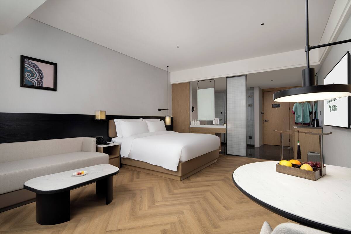 Ein modernes Hotelzimmer mit Bett, Sofa, Nachttisch und einem kleinen Esstisch mit Obst.