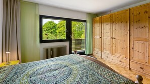 Ein Schlafzimmer mit einem großen Bett, einem Holzschrank, einer Heizung und einem Fenster mit Blick auf Grünflächen.