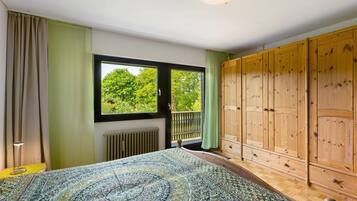 Ein Schlafzimmer mit einem großen Bett, einem Holzschrank, einer Heizung und einem Fenster mit Blick auf Grünflächen.