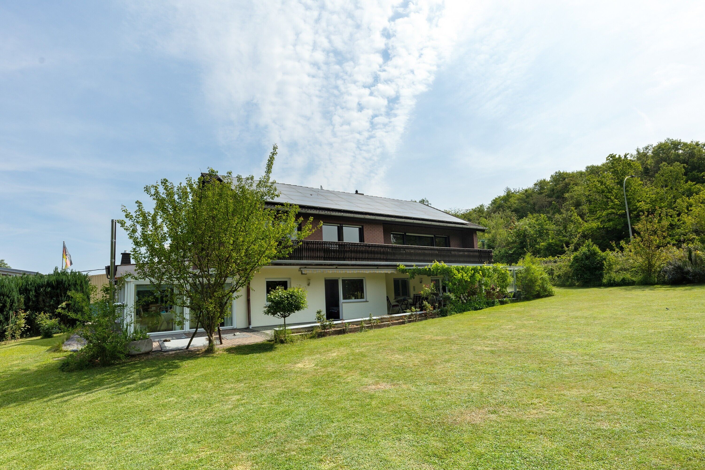 Ein zweistöckiges Haus mit Balkon, umgeben von einem gepflegten Rasen und Bäumen.