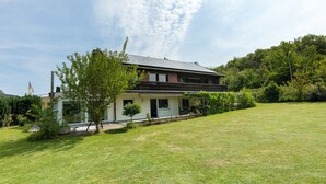 Ein zweistöckiges Haus mit Balkon, umgeben von einem gepflegten Rasen und Bäumen.