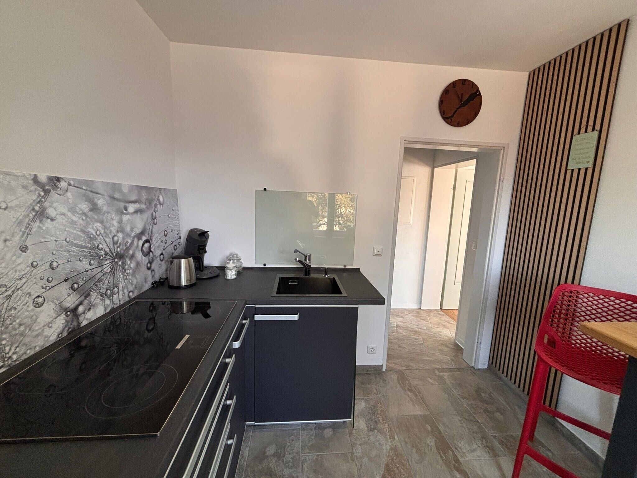 A modern kitchen with a black countertop, stainless steel appliances, a small island, and a red chair.