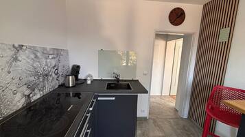 A modern kitchen with a black countertop, stainless steel appliances, a small island, and a red chair.