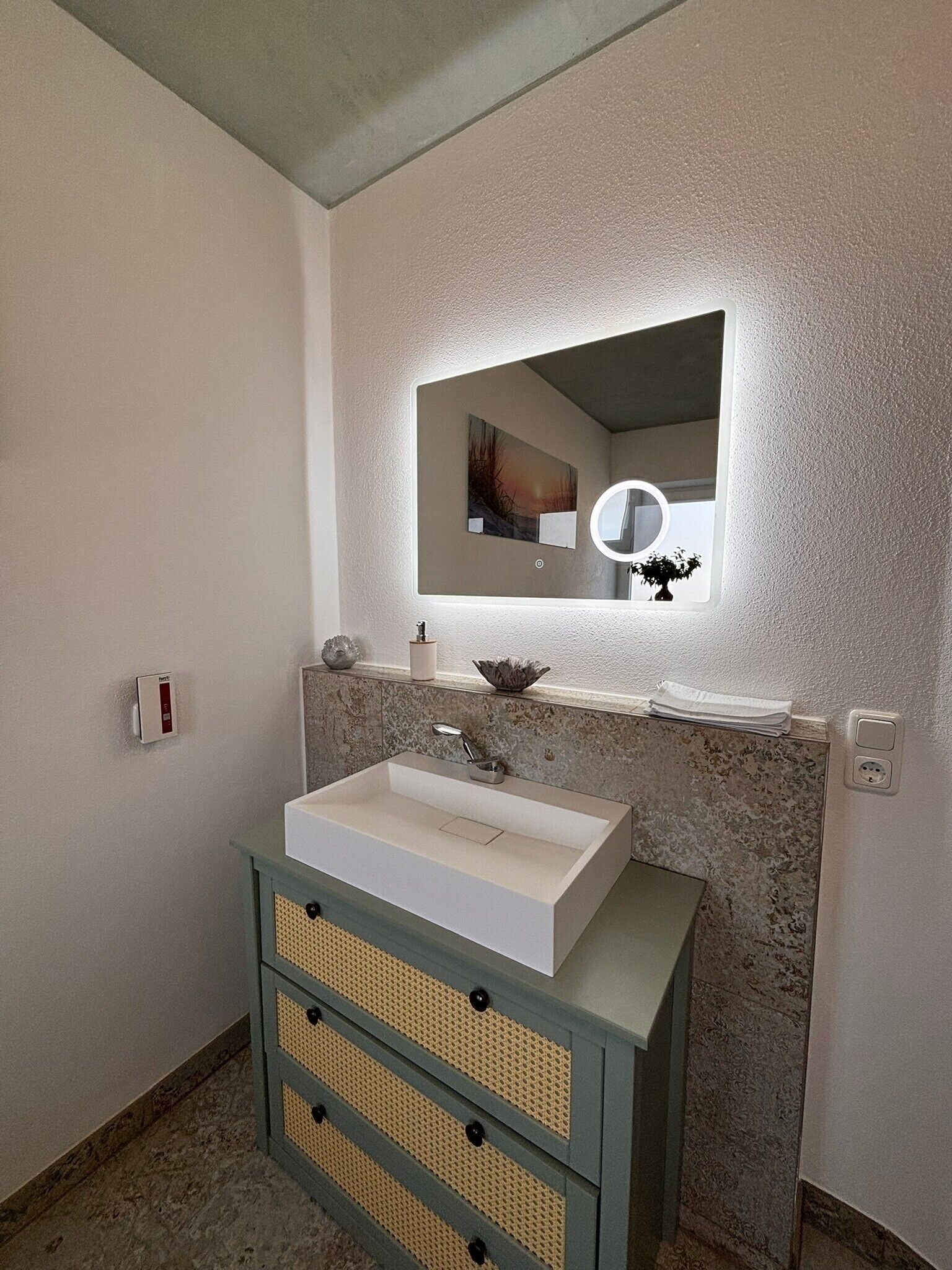 Ein Badezimmer mit einem rechteckigen Waschbecken, einem Spiegel darüber und einer strukturierten Wand.