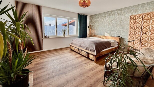 A bedroom with a wooden bed, a window with a view, a geometric-patterned wall, and a ceiling light fixture. - Apartment 'Dandelion' with Private Terrace and Wi-Fi (Haag)