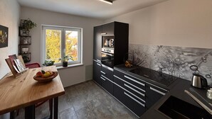 A modern kitchen with a wooden table, black cabinets, and a window with a view of trees. - Apartment 'Dandelion' with Private Terrace and Wi-Fi (Haag)
