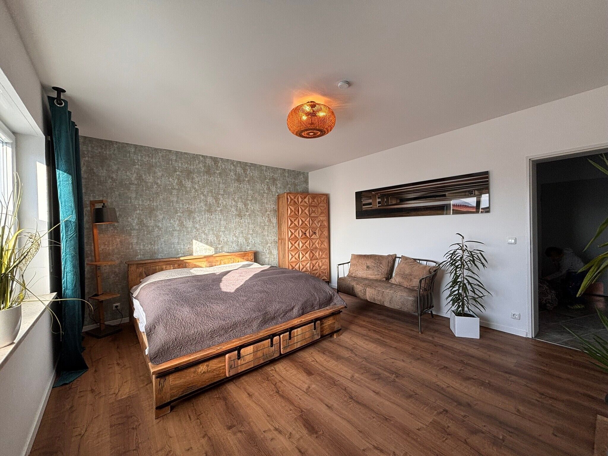 A bedroom with a wooden bed, a sofa, a floor lamp, and a wall-mounted TV.