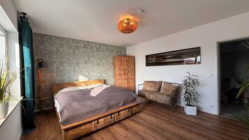 A bedroom with a wooden bed, a sofa, a floor lamp, and a wall-mounted TV.
