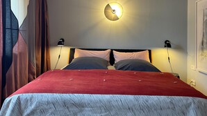 Ein Schlafzimmer mit einem Bett, zwei Nachttischlampen, einer Wandleuchte und einem Fenster mit Vorhängen.