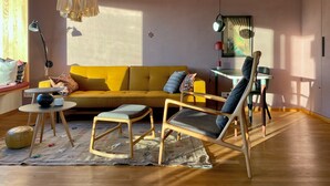 Ein Wohnzimmer mit gelber Couch, Holzboden und einem Tisch mit Lampe.