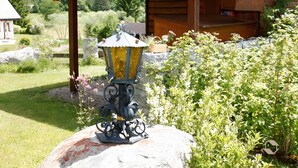 A wooden cabin with a covered porch, a decorative lantern, and a garden with various plants and flowers. - Holiday Apartment 'Type B, 70sqm' with Mountain View, Private Terrace and Wi-Fi (Schluchsee)