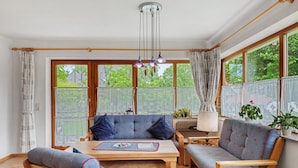 A cozy room with a sofa, chairs, a table, and large windows with curtains. - Holiday Apartment 'Type B, 70sqm' with Mountain View, Private Terrace and Wi-Fi (Schluchsee)