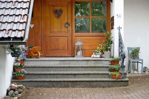 A wooden door with a heart decoration, a set of stone steps leading to a door, and potted plants on either side.
