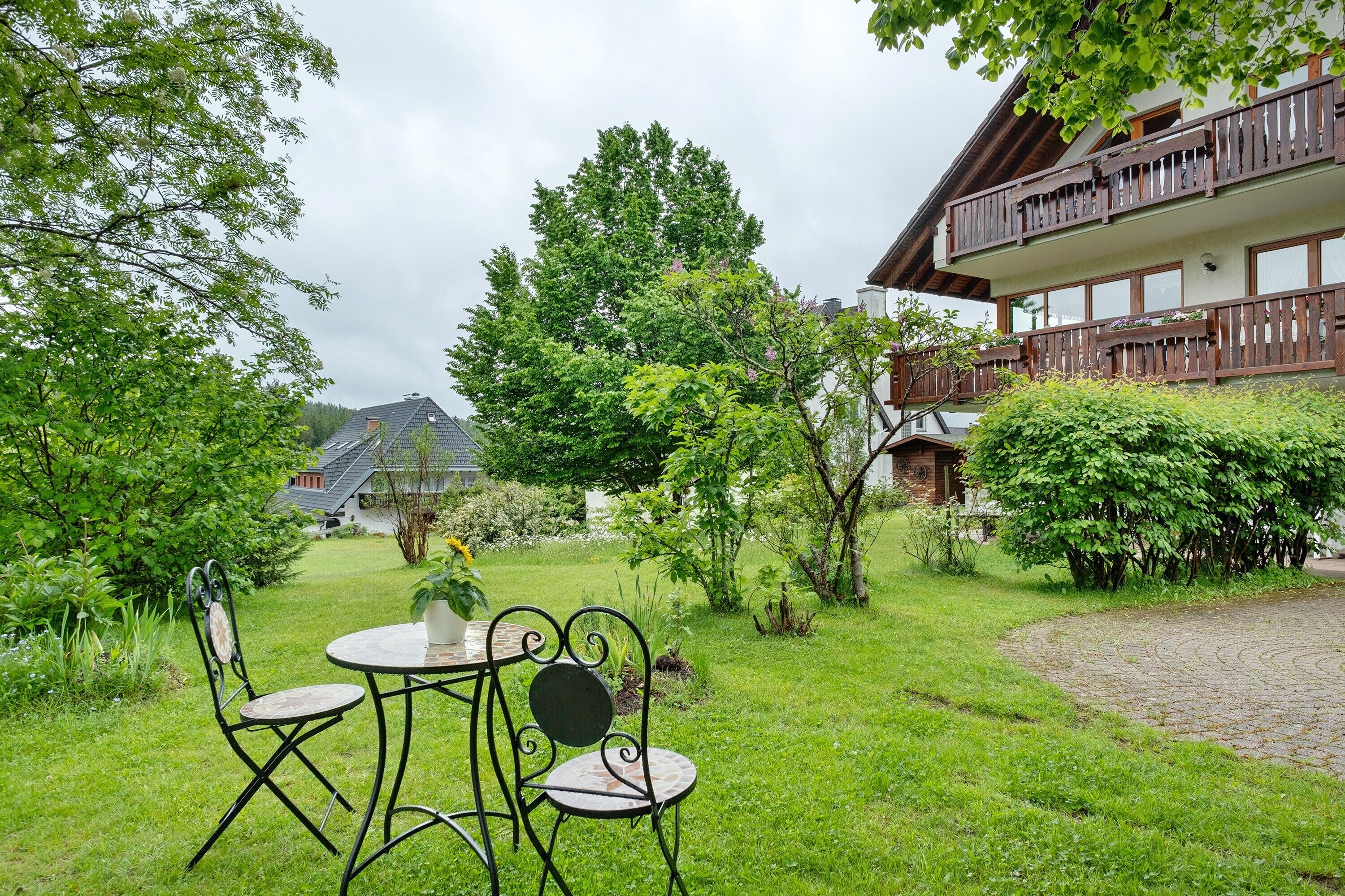 A garden with a table and chairs, a building with a balcony, and a tree.