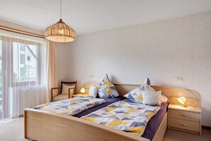 Une chambre à coucher avec un lit, des tables de chevet, une chaise et une fenêtre avec des rideaux légers.