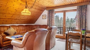 A cozy living room with a brown leather sofa, wooden dining table, and a hanging light fixture.