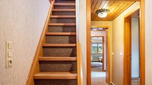 A wooden staircase with carpeted steps leading to a hallway with wooden walls and a ceiling light fixture.