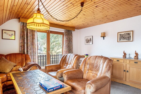 A living room with leather sofas, a wooden ceiling, a table with a board game, and a wooden cabinet with decorative items.