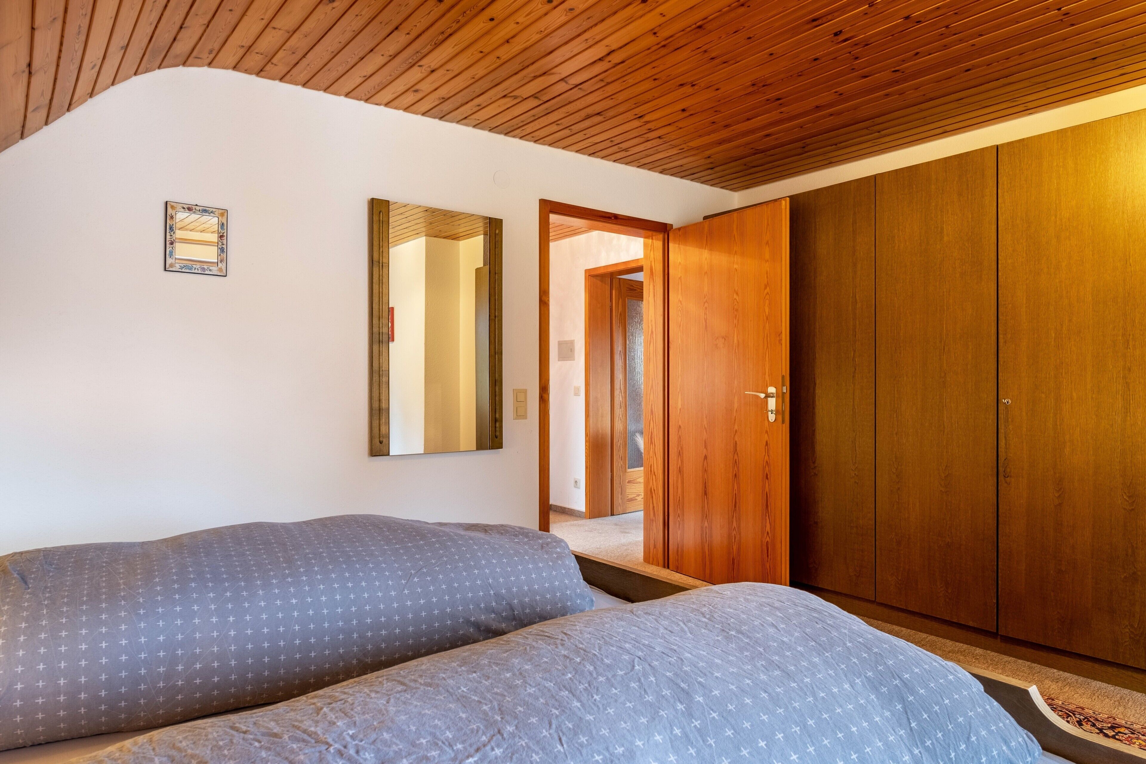 Un dormitorio con dos camas, un armario de madera, un espejo y una puerta que da a otra habitación.