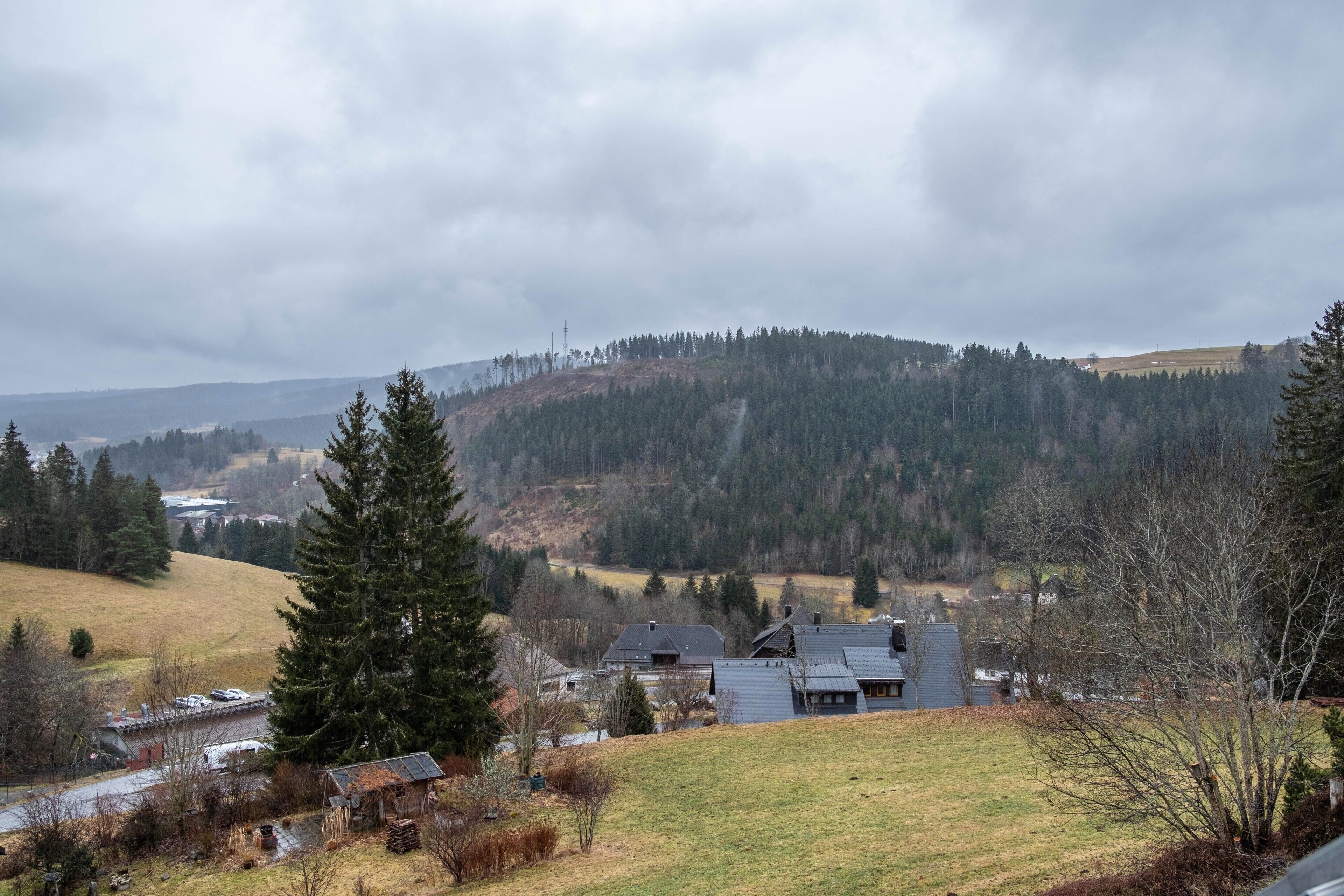 Paisaje rural con una casa, un edificio pequeño y una colina con árboles.